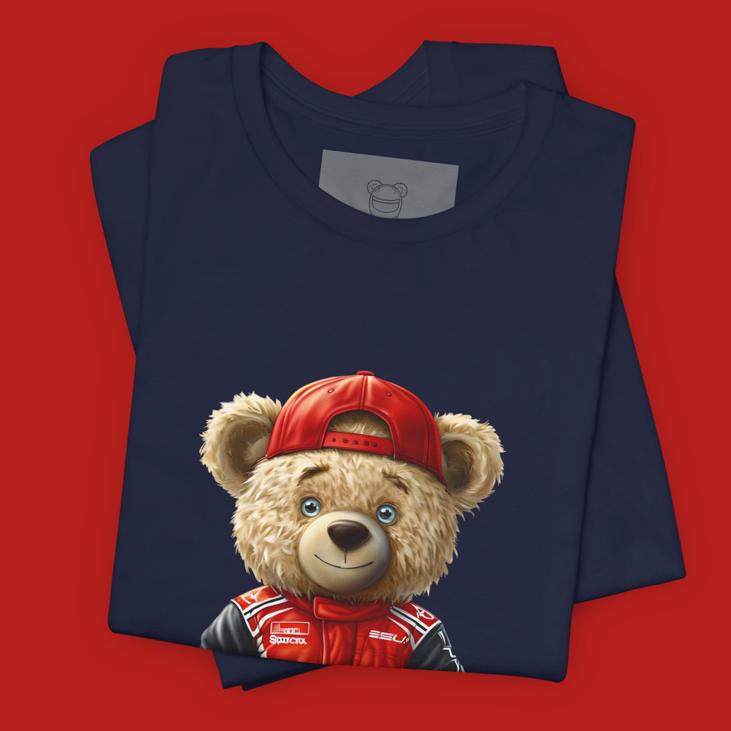 A teddy bear wearing a red karting suit with black accents and name patch "Champ", and a backwards worn red cap on a navy unisex t-shirt